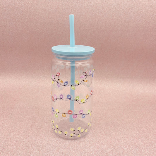 Clear tumbler with colorful light string design and blue straw on a pink background