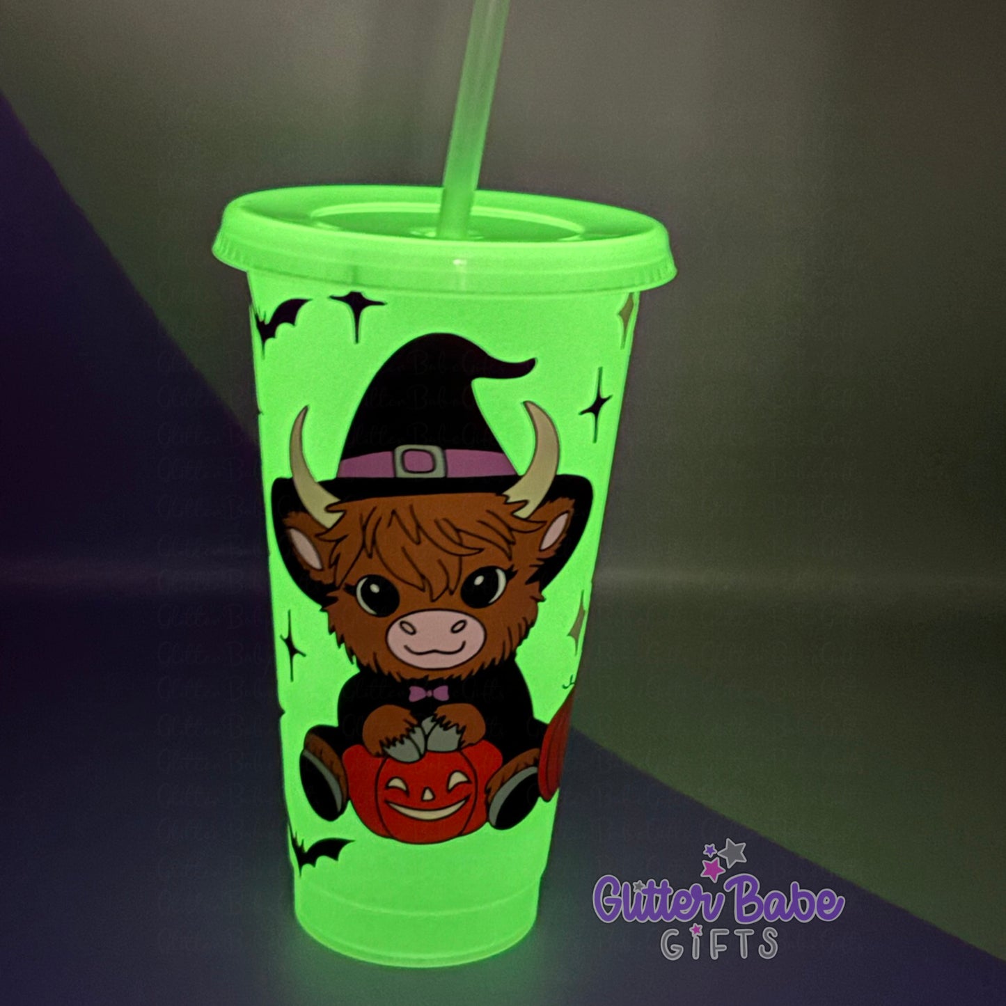 Glowing green tumbler with a cow wearing a witch hat and pumpkin design, on a dark background.