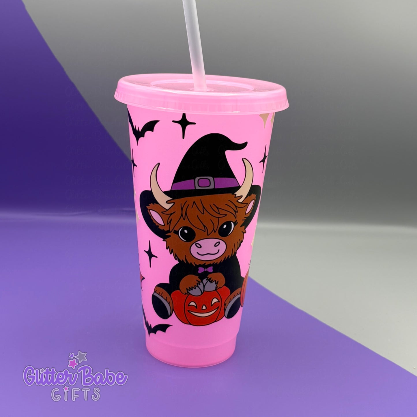 Glowing Pink tumbler with a cartoon cow wearing a witch hat and holding a pumpkin on a grey and purple gradient background.
