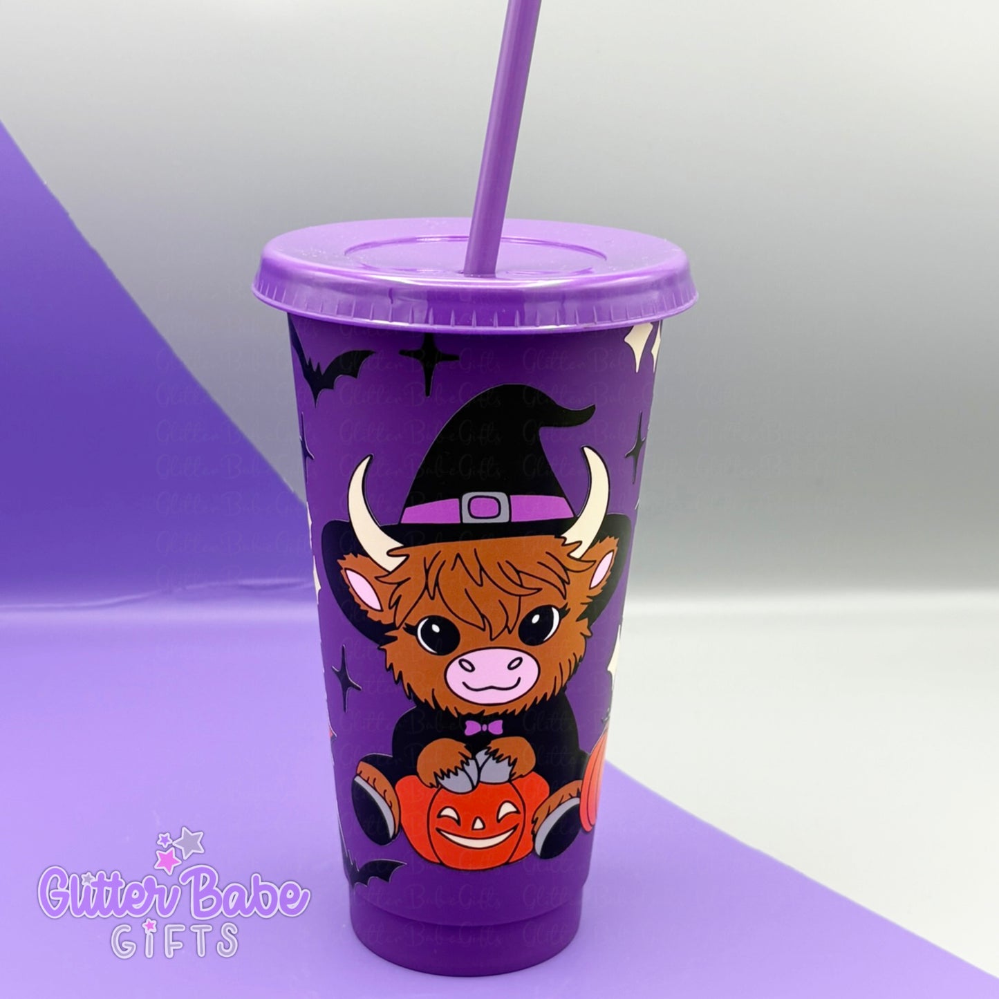 Purple tumbler with a cow wearing a witch hat and sitting with a pumpkin, on a purple and grey background.