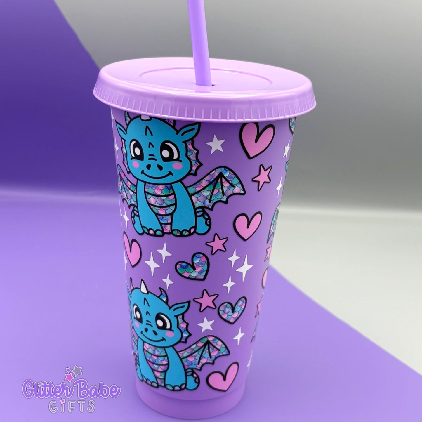 A Lavender coloured tumbler with blue dragon with rainbow scales, Pink hearts and white and pink stars design on a purple and grey backdrop