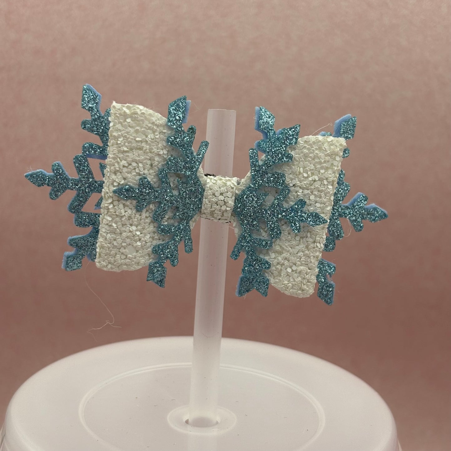 White and blue bow with snowflake shape straw topper attached to clear straw against a pink background