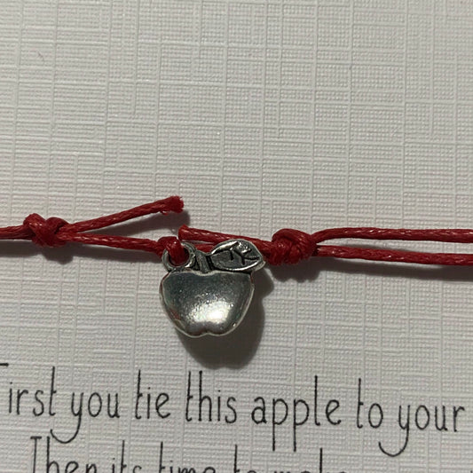 close up of a silver apple charm on red cord with some text below it in black