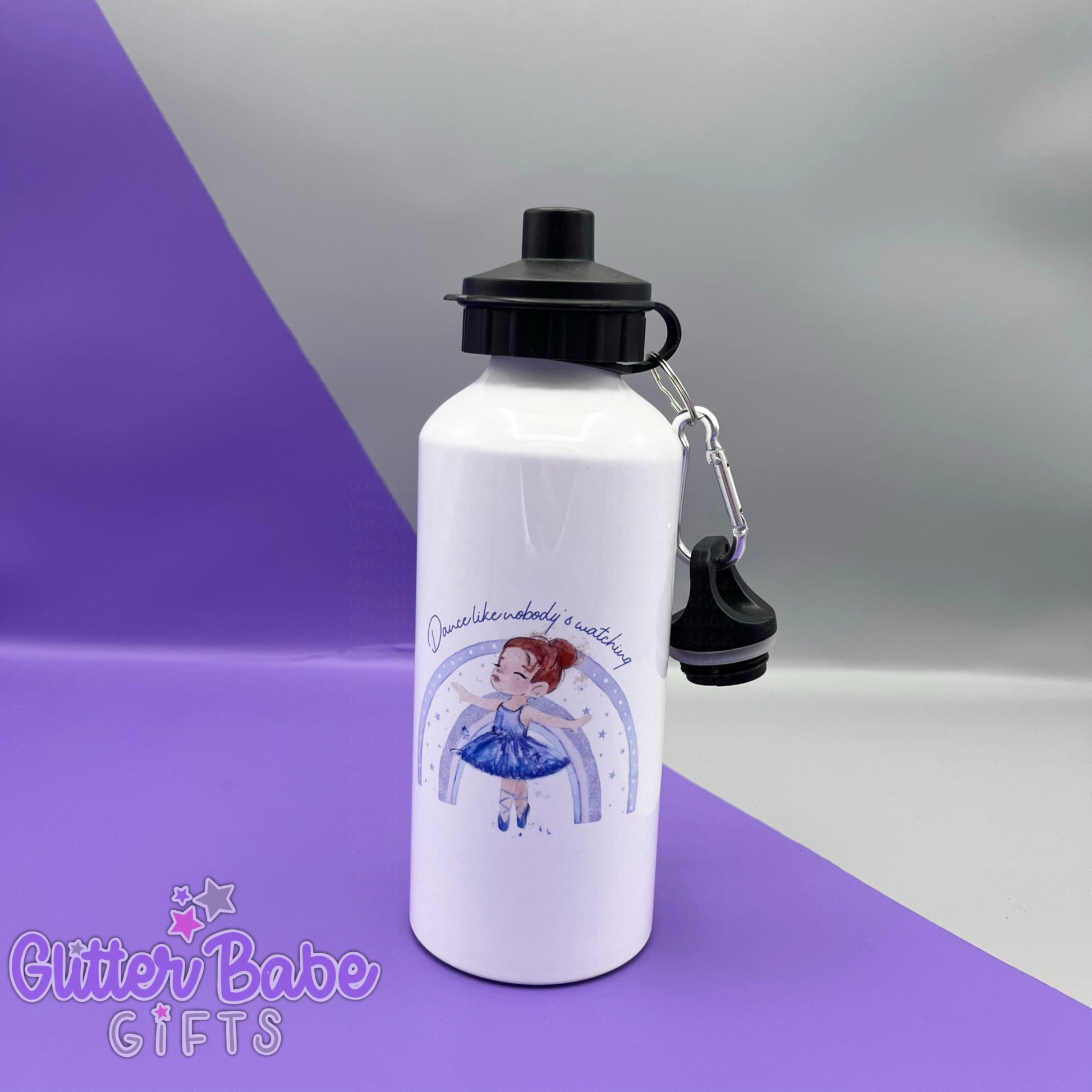 a white drinks bottle with two black lids against a purple and grey backdrop. Bottle has a redhaired ballerina wearing lilac stood in front of a rainbow and some text above image printed on to the front. 