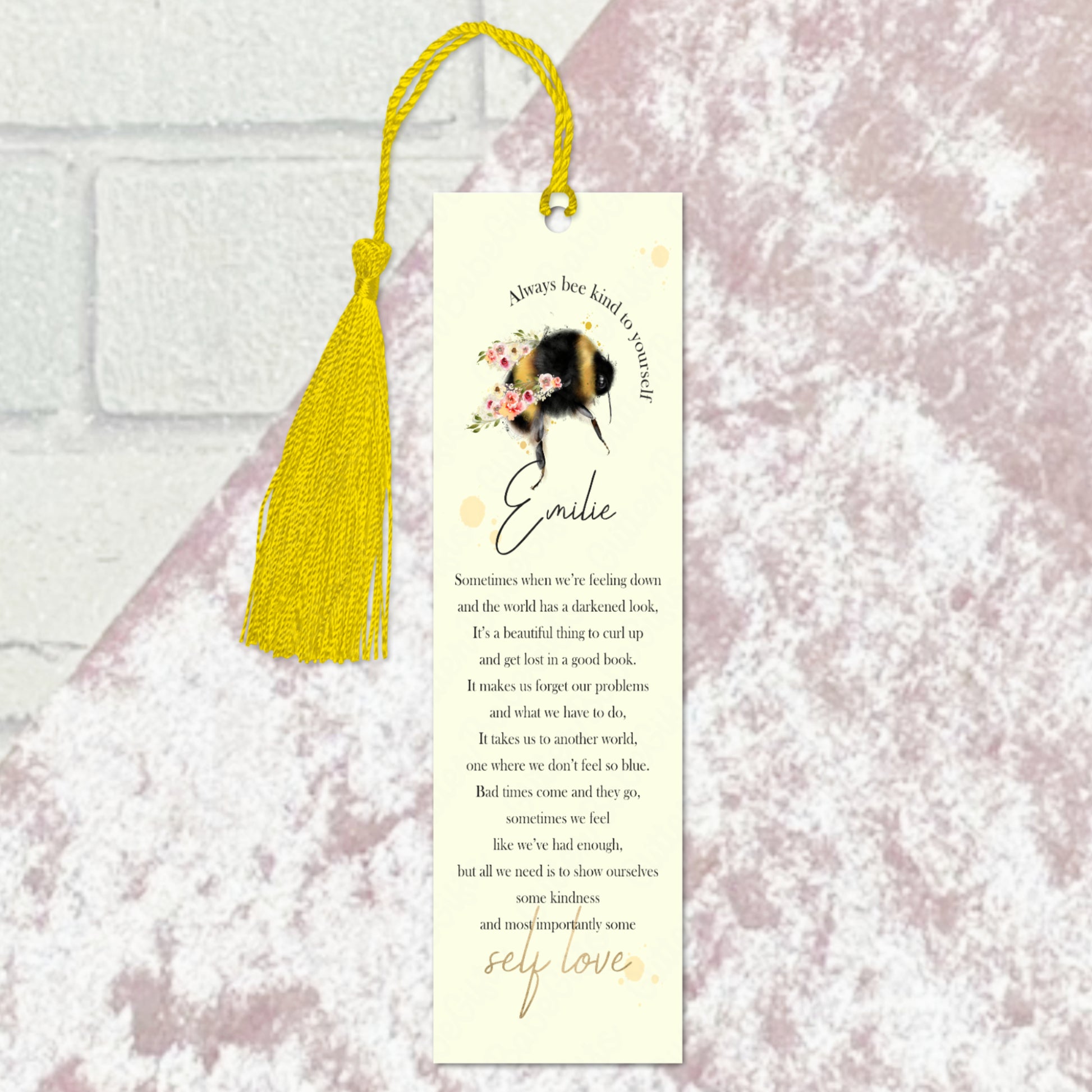 Bookmark with yellow tassel and bee design with wording and a name against a pale pink background