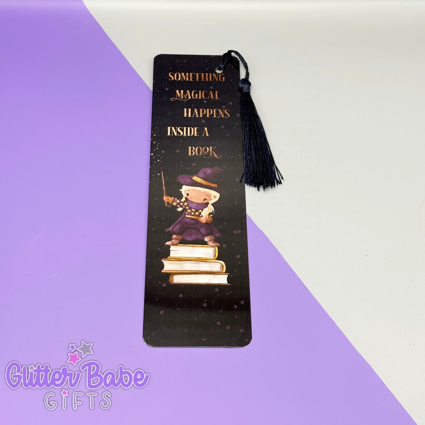 Bookmark with tassel. the bookmark has a girl wizard with blonde hair printed on it. bookmark lays on purple and grey background.