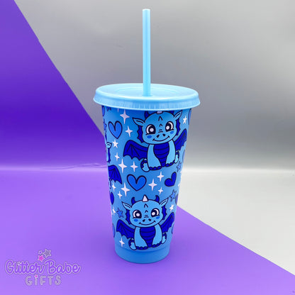 A blue tumbler with two shades of blue dragon , blue hearts and white and blue stars design on a purple and grey backdrop