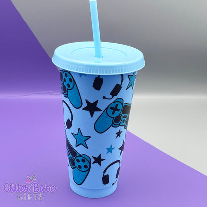 a light blue coloured cold cup with blue and black coloured gaming controller themed pattern against a purple and grey backdrop