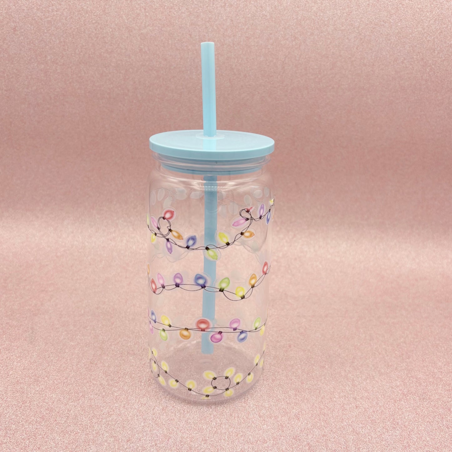 Clear tumbler with colorful light string design and blue straw on a pink background