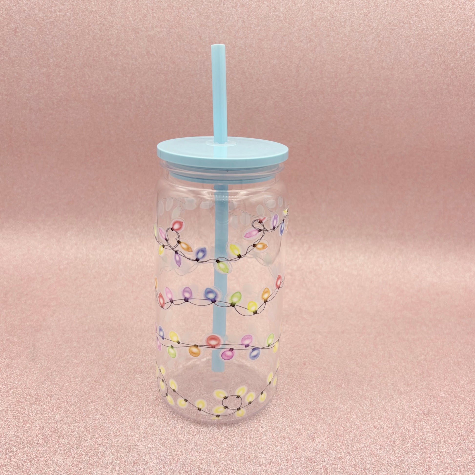 Clear tumbler with colorful light string design and blue straw on a pink background