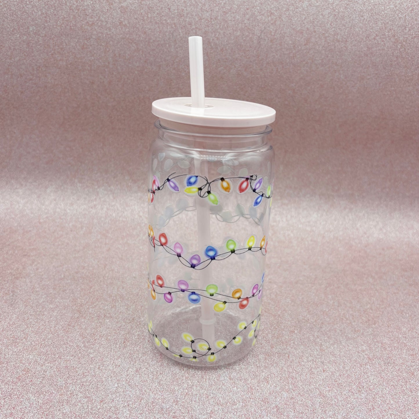 Clear tumbler with colorful string lights design and white lid and straw on a light pink background
