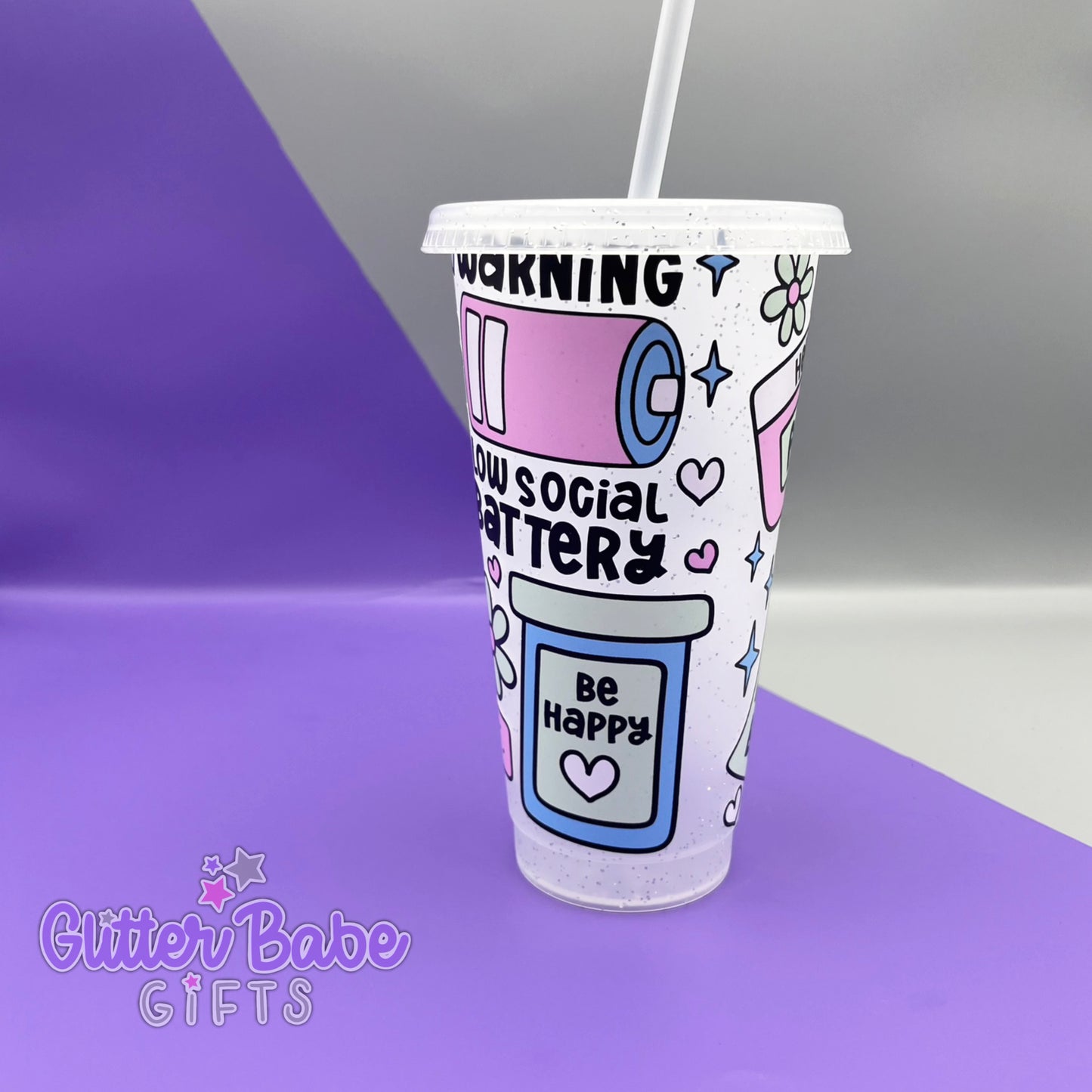 A frosted glitter cold cup showing a warning low social battery image with hearts and stars, Cup is on a  purple and grey background. 