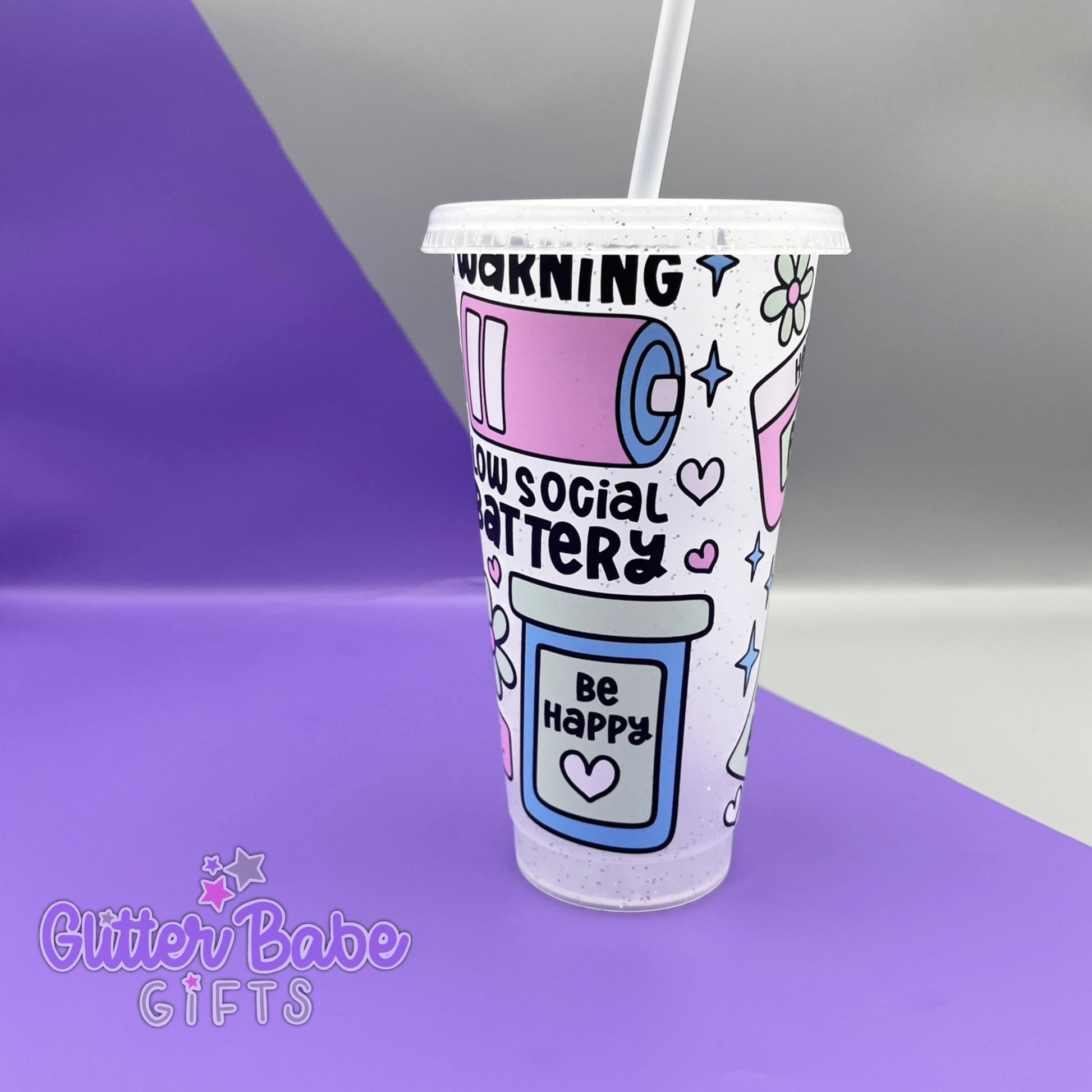A frosted glitter cold cup showing a warning low social battery image with hearts and stars, Cup is on a  purple and grey background. 
