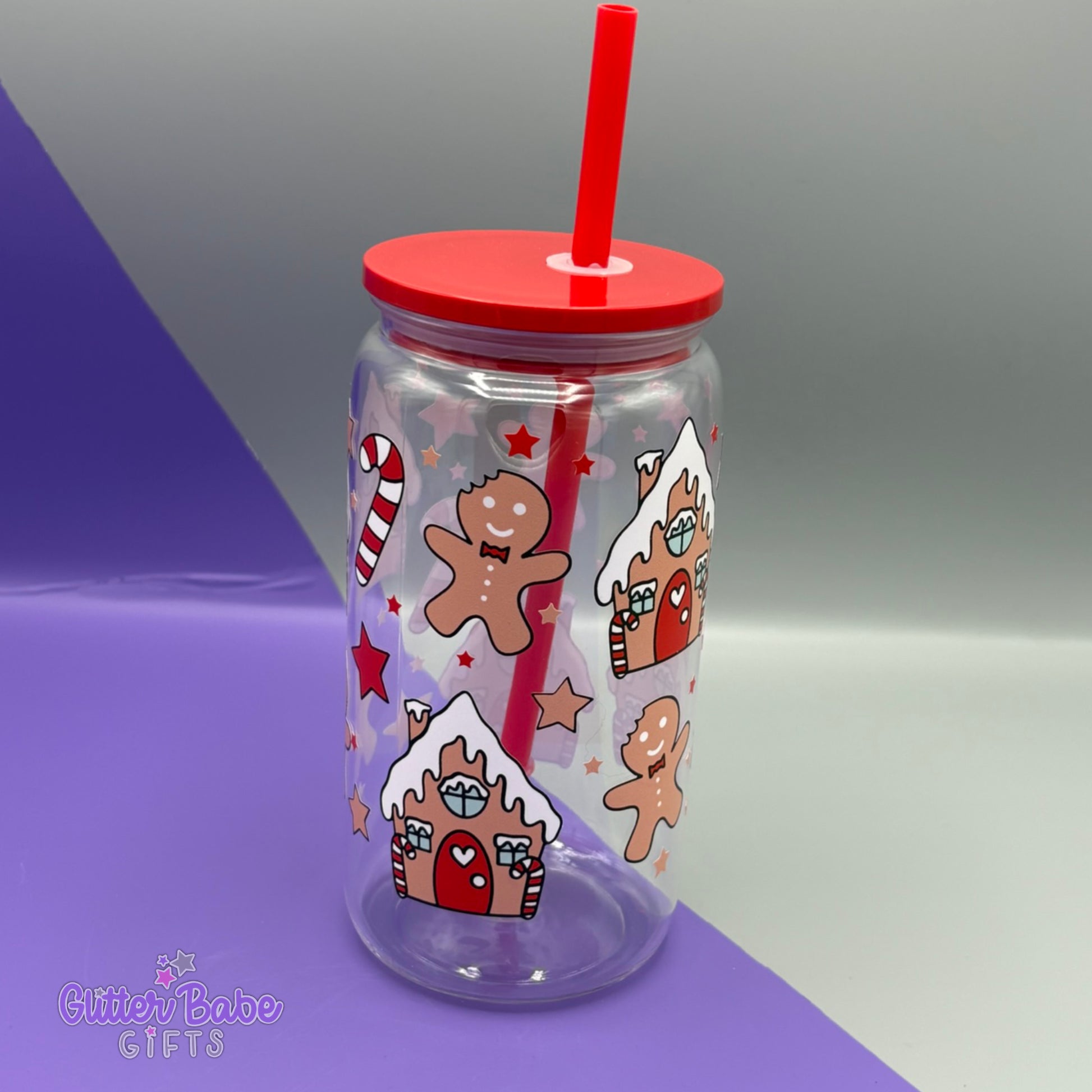 Clear tumbler with gingerbread man and house design, red lid and straw on a gradient background.