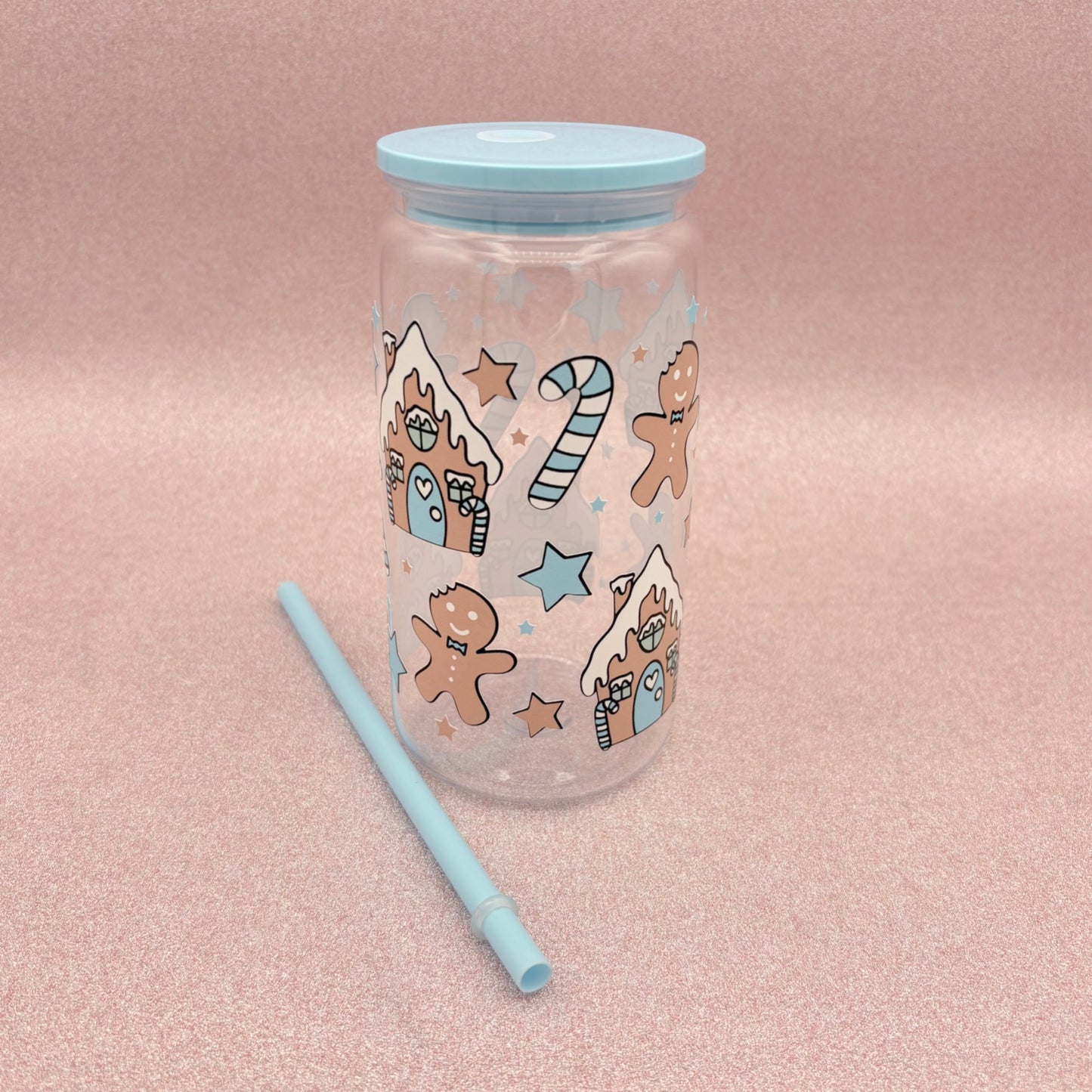 Clear tumbler with gingerbread man design and blue lid and straw on a pink background