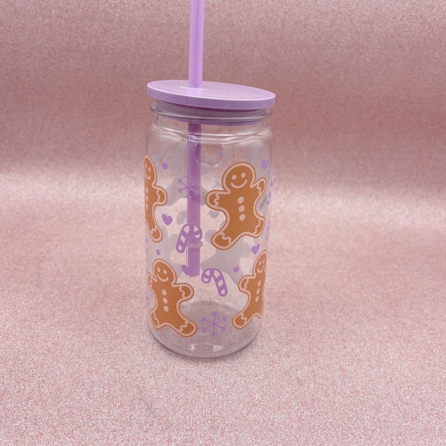 Clear tumbler with gingerbread man design and purple straw on a pink background