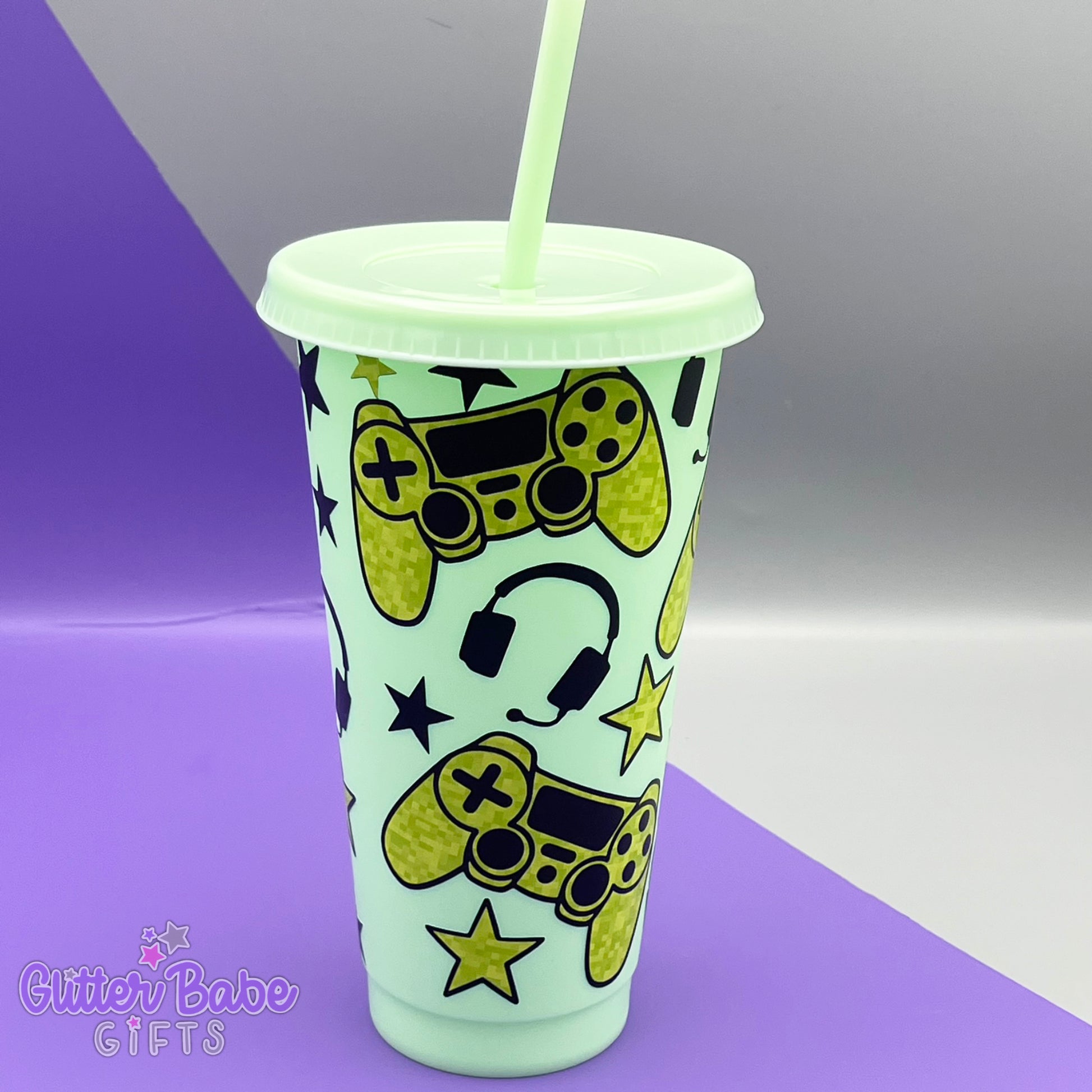 a mint coloured cold cup with green and black coloured gaming controller themed pattern against a purple and grey backdrop