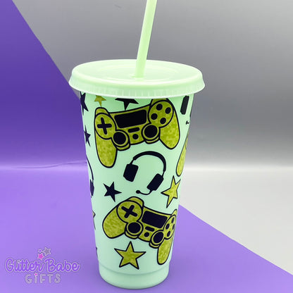 a mint coloured cold cup with green and black coloured gaming controller themed pattern against a purple and grey backdrop