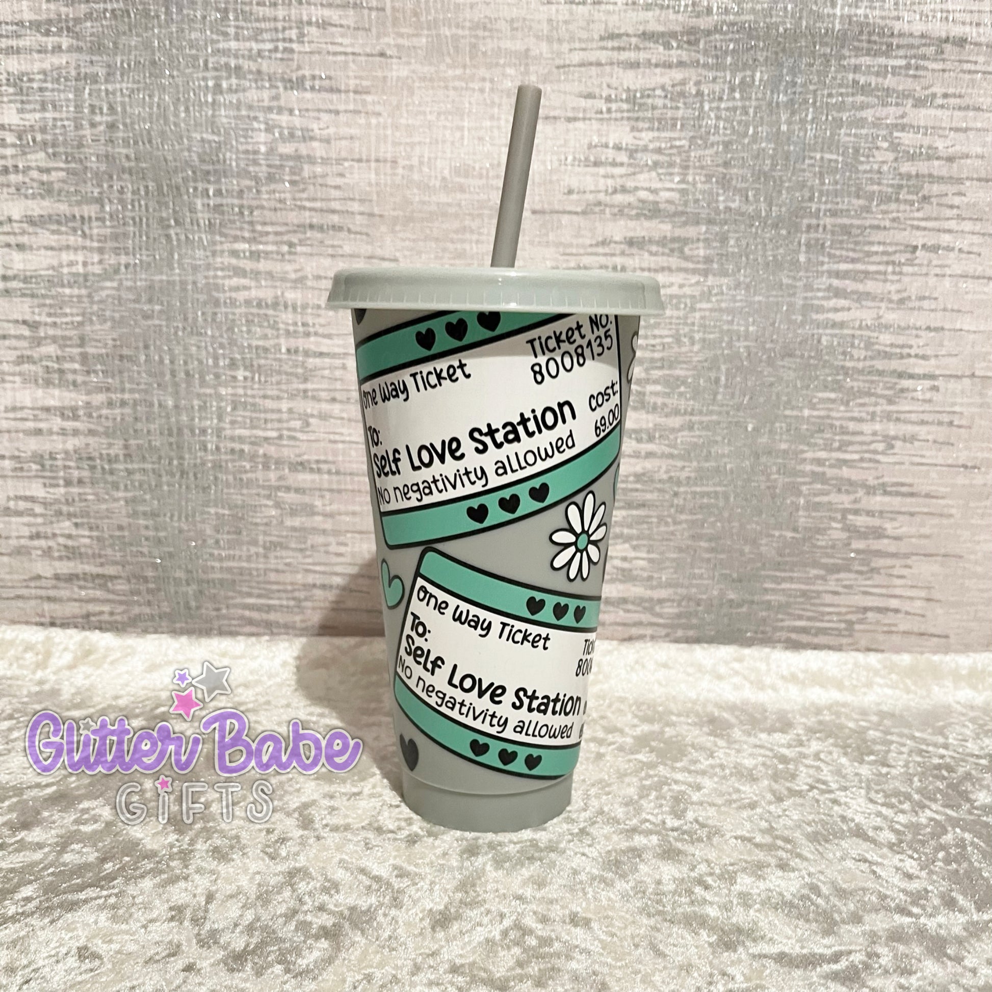 A grey cold cup with a travel ticket style pattern and the text 'Self Love Station' printed on it.