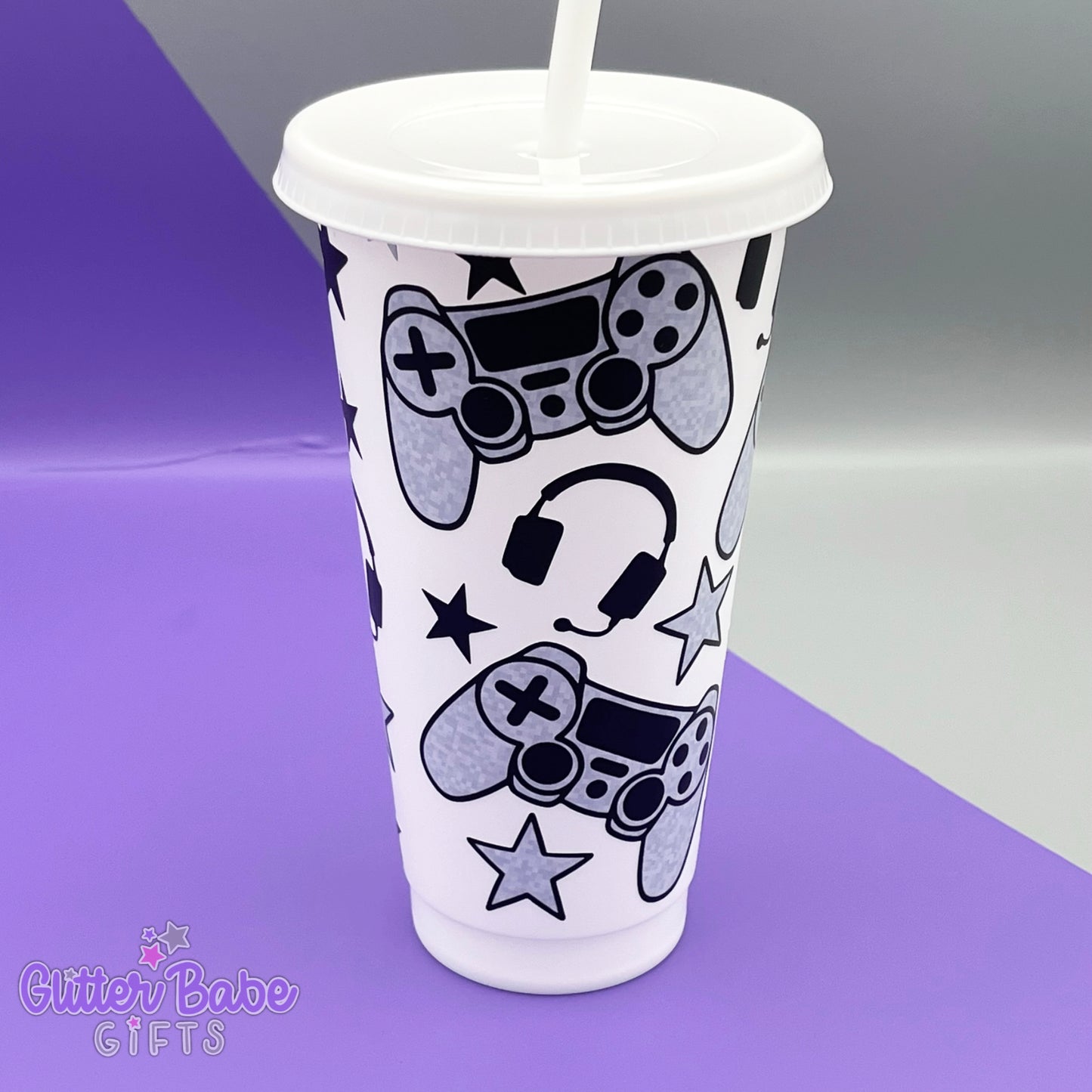  A white coloured cold cup with grey and black coloured gaming controller themed pattern against a purple and grey backdrop