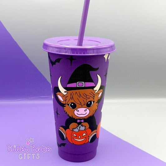 Purple tumbler with a cow wearing a witch hat and sitting with a pumpkin, on a purple and grey background.