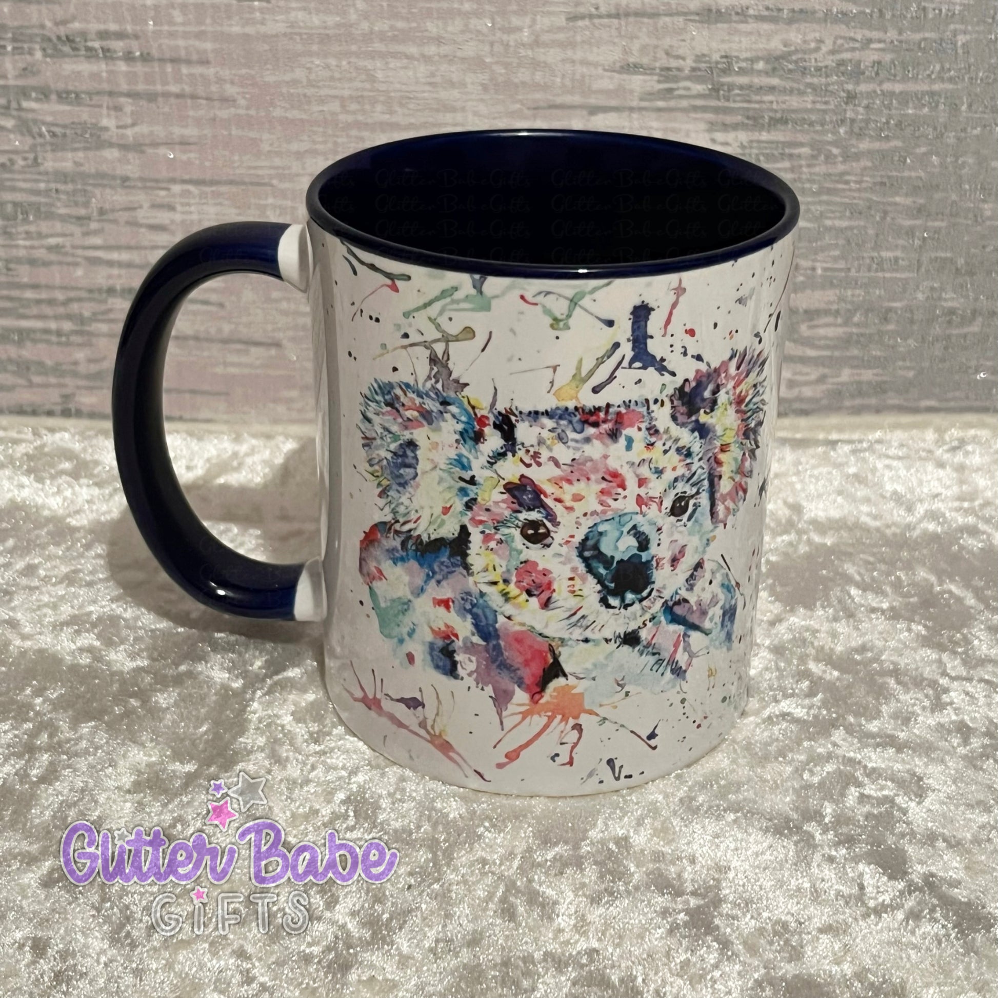 A ceramic mug with a multicolored koala design on the front, with a dark blue inner surface and handle, displayed on a textured background.