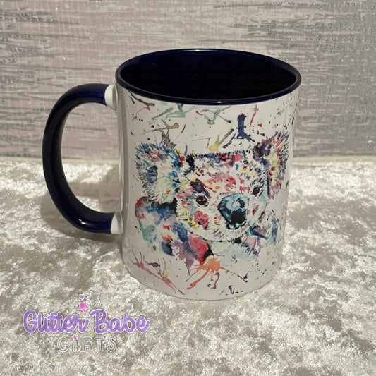 A ceramic mug with a multicolored koala design on the front, with a dark blue inner surface and handle, displayed on a textured background.