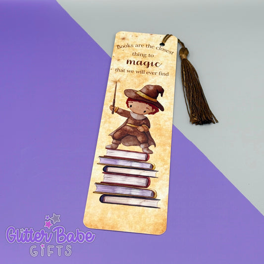 a bookmark with a wizard stood n bookstack design with the wording "Books are the closest thing to magic that we will ever find". the bookmark has a bronze coloured tassel and lays upon a purple and grey background.