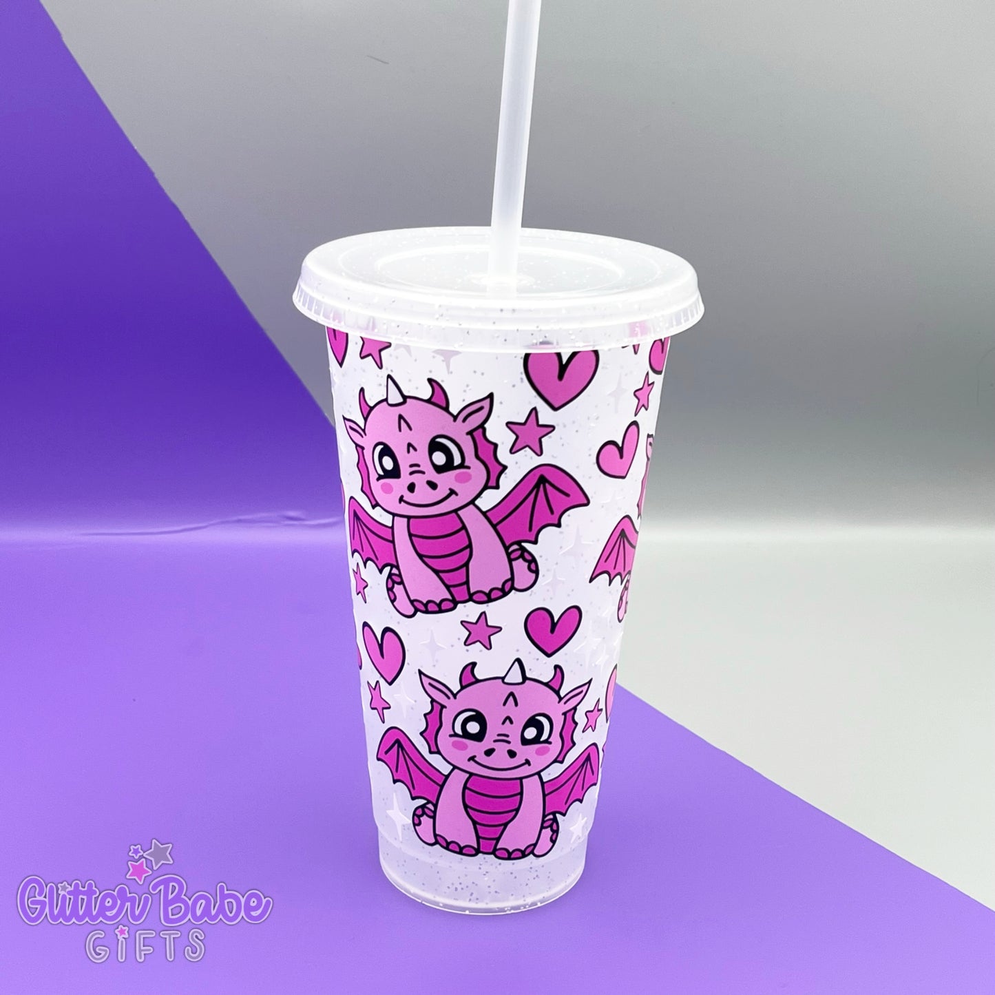 a clear with silver glitter tumbler with pink dragon designs with pink hearts and white and pink stars on a purple and grey backdrop