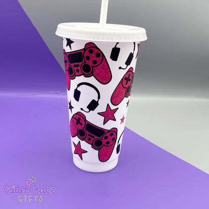 a white coloured cold cup with  a dark pink and black coloured gaming controller themed pattern against a purple and grey backdrop