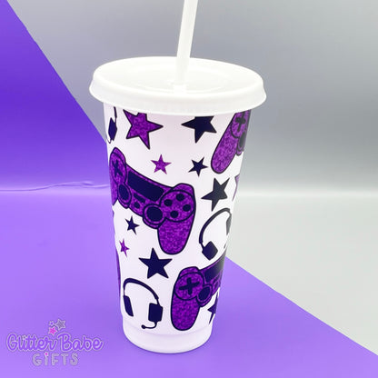 a white coloured cold cup with purple and black coloured gaming controller themed pattern against a purple and grey backdrop