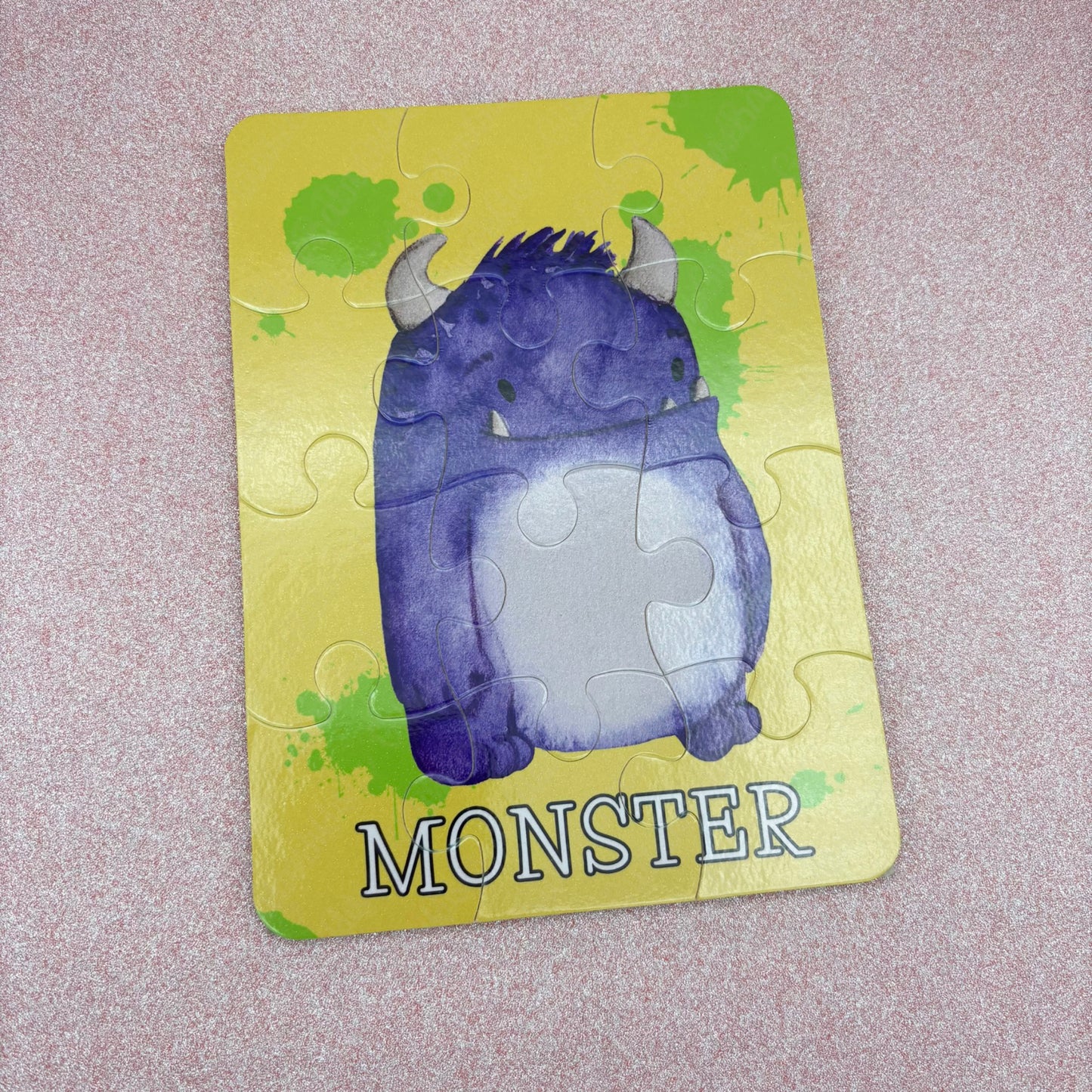 Jigsaw puzzle piece with a purple monster illustration on a yellow background - puzzle is laying against a pink backdrop