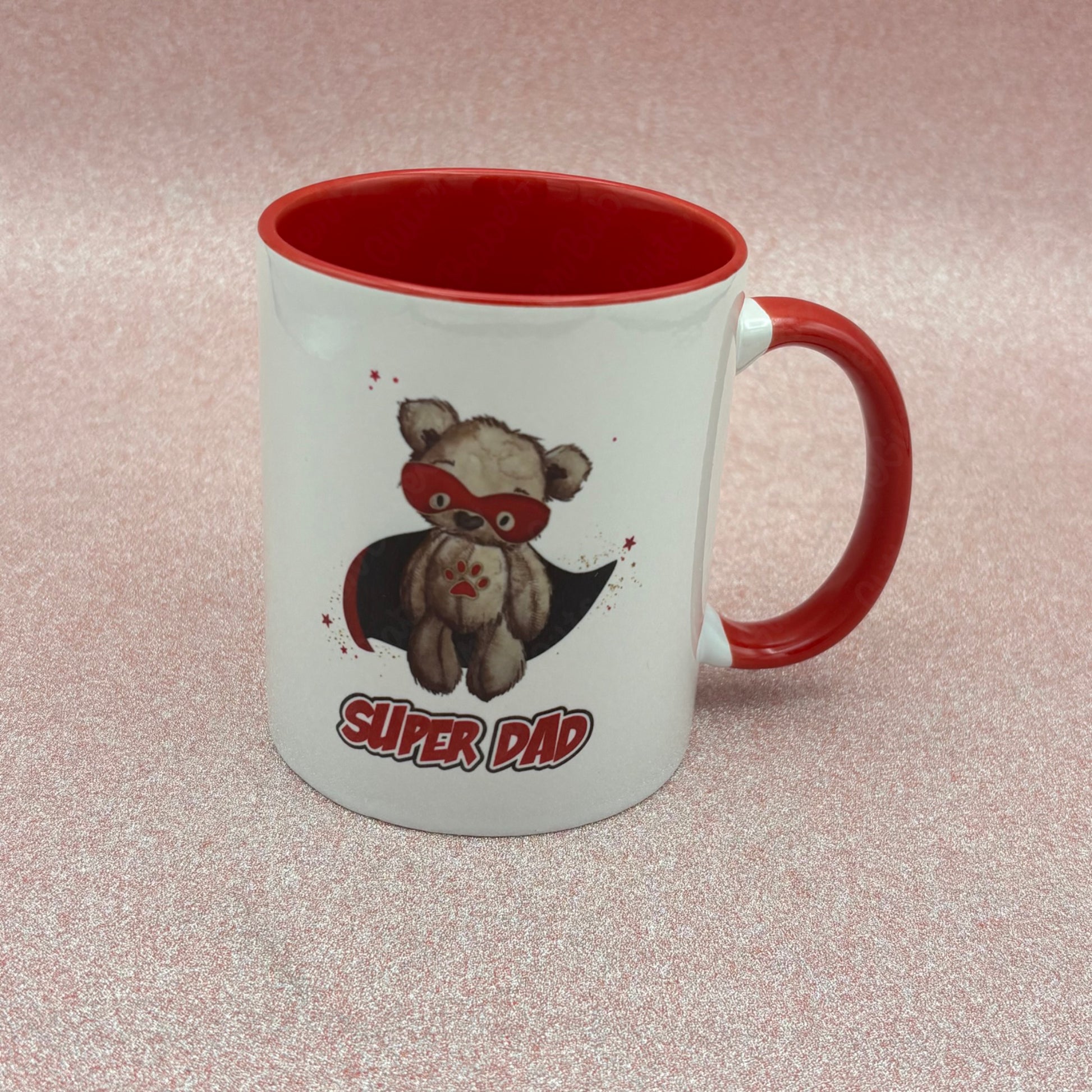 White Mug with red inner and handle with a teddy bear wearing a superhero costume and 'Super Dad' text on a pink  background