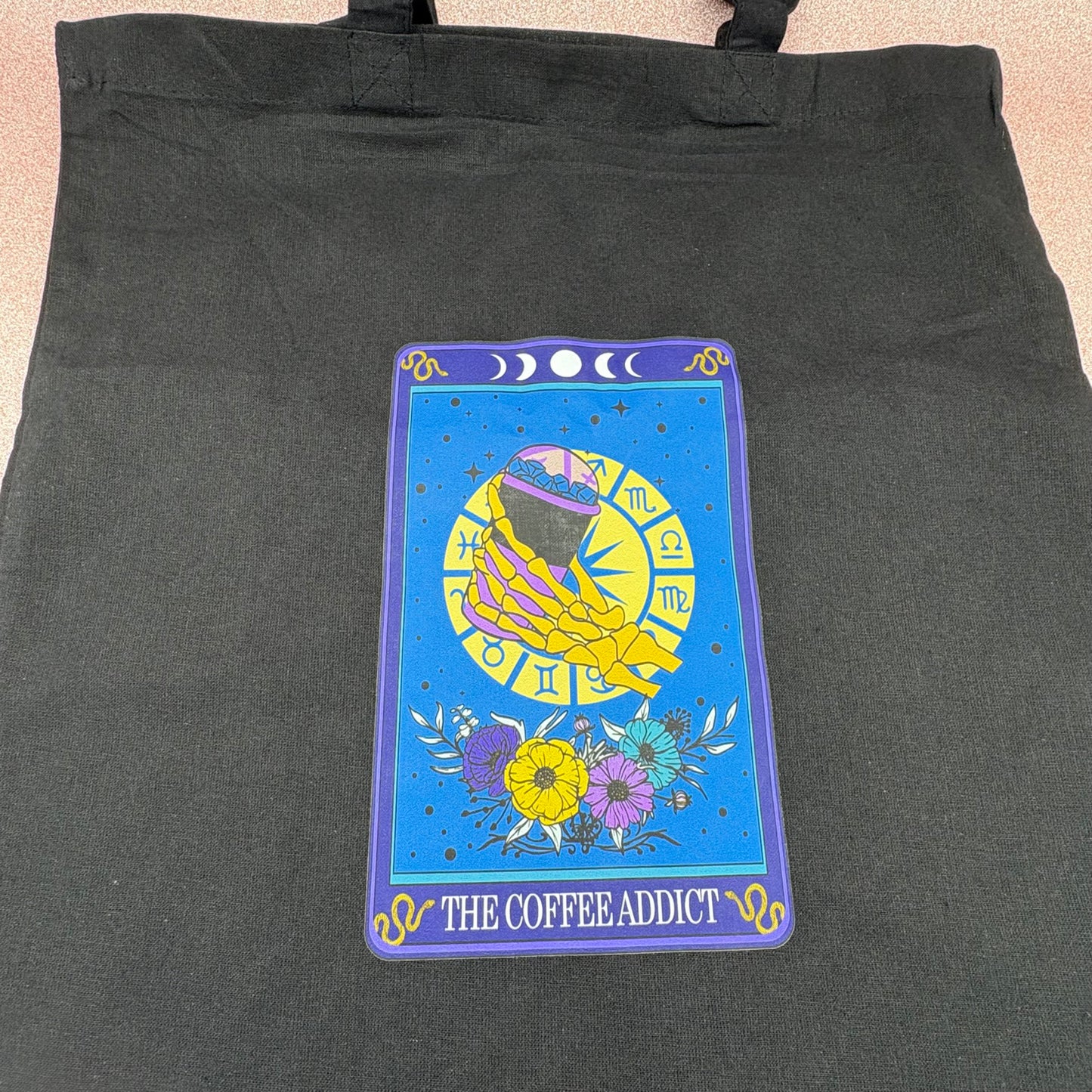 Black tote bag with a colorful tarot card design featuring 'The Coffee Addict' text.
