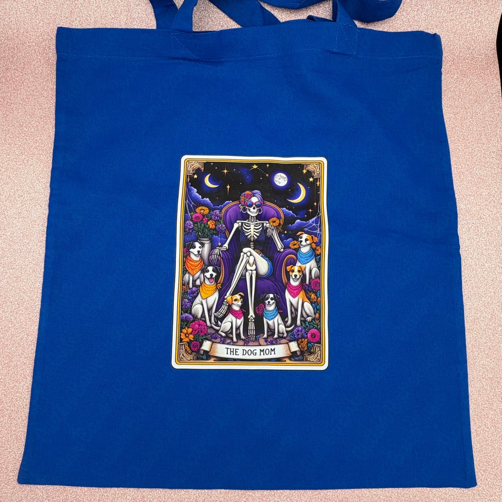 Blue tote bag with a graphic design of a skeleton and dogs on a pink surface