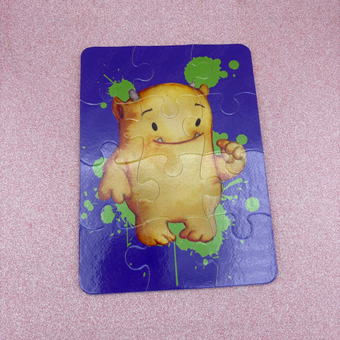 Children's puzzle with a yellow cartoon monster character on a purple background laying against a pink surface