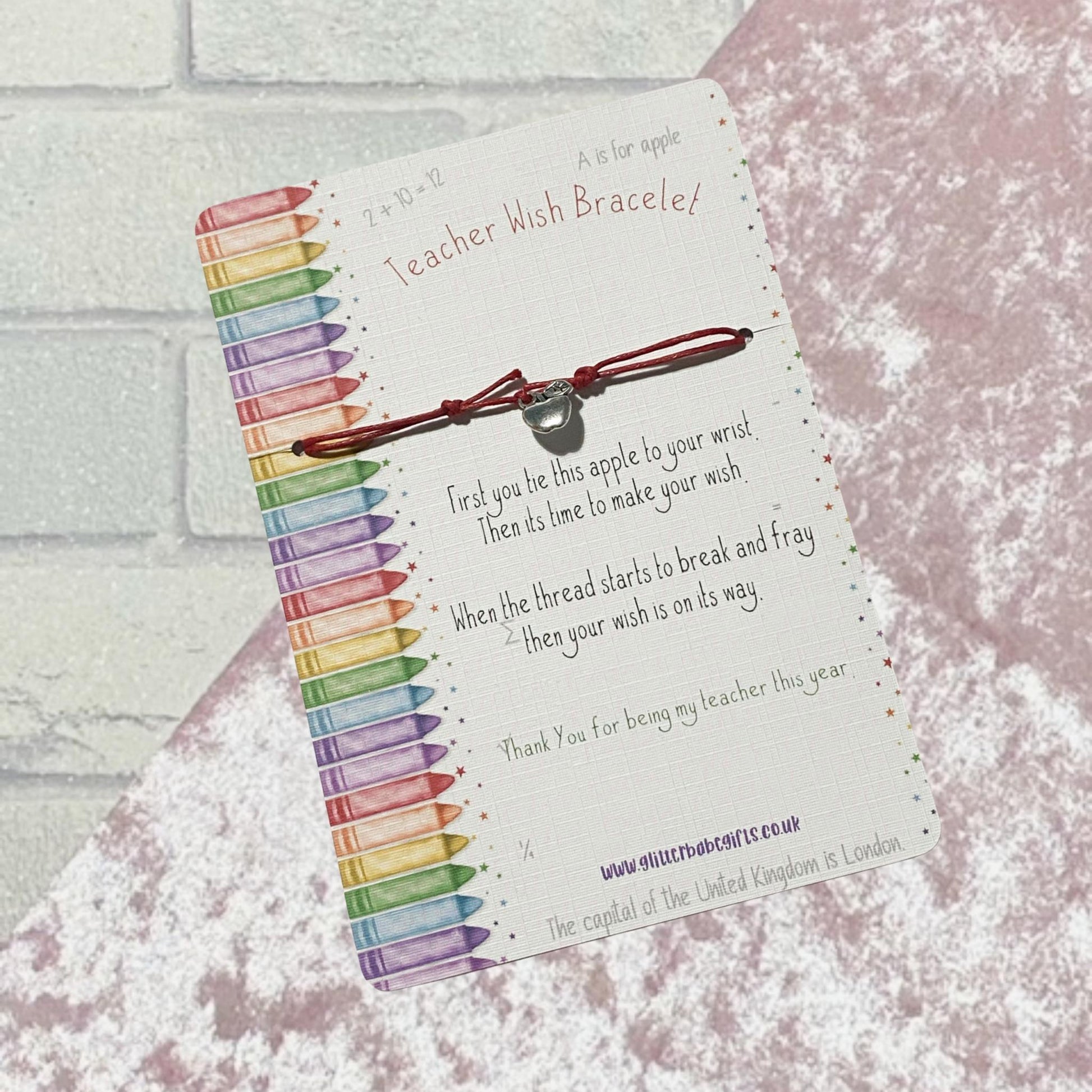 Red cord wish bracelet with silver coloured apple charm on a backing card that features colourful crayons and little poem